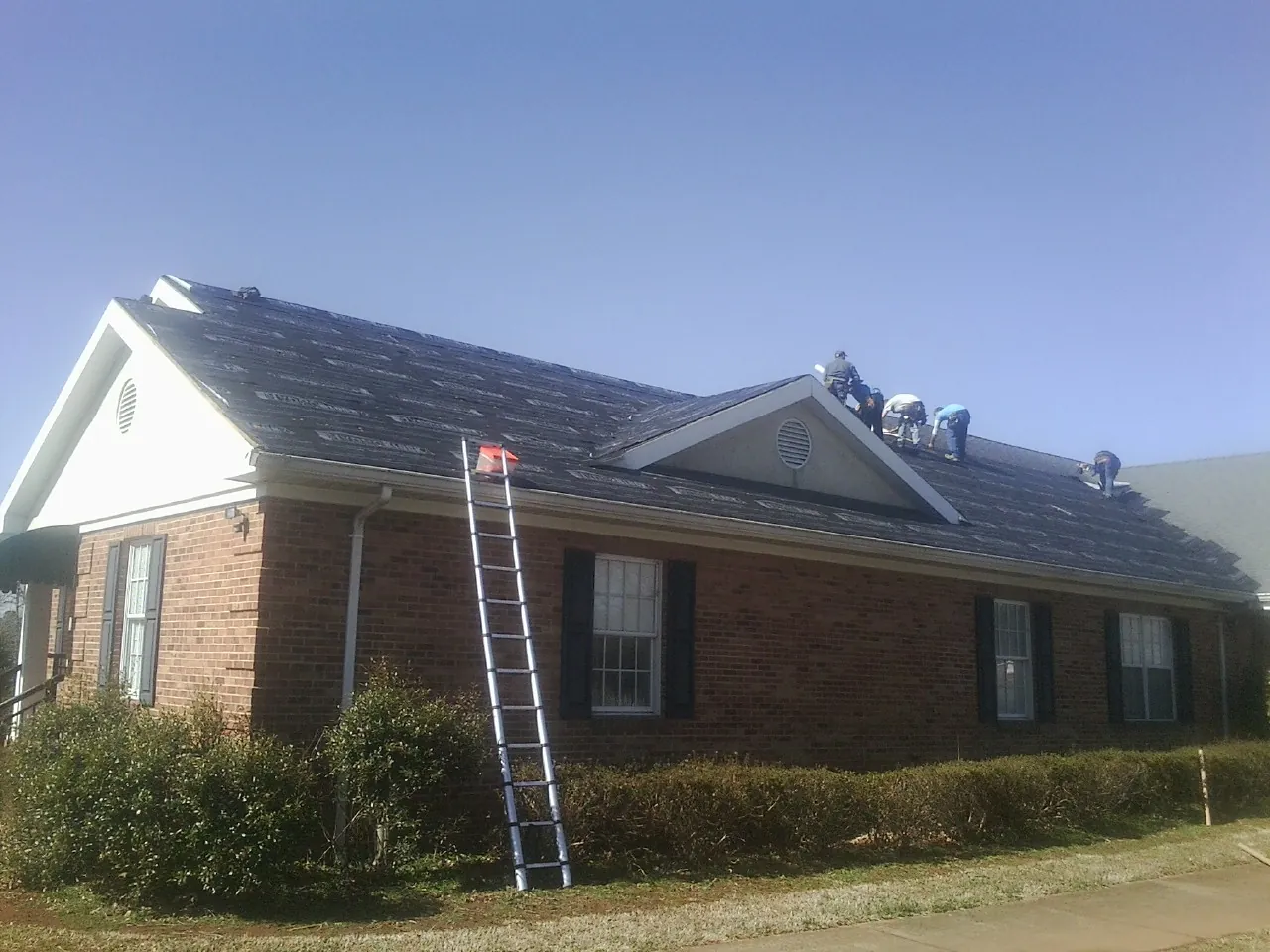 Crew tearing shingles off a brick ranch roof with a ladder set — Emergency Roof Repair work by our crew in Unicoi