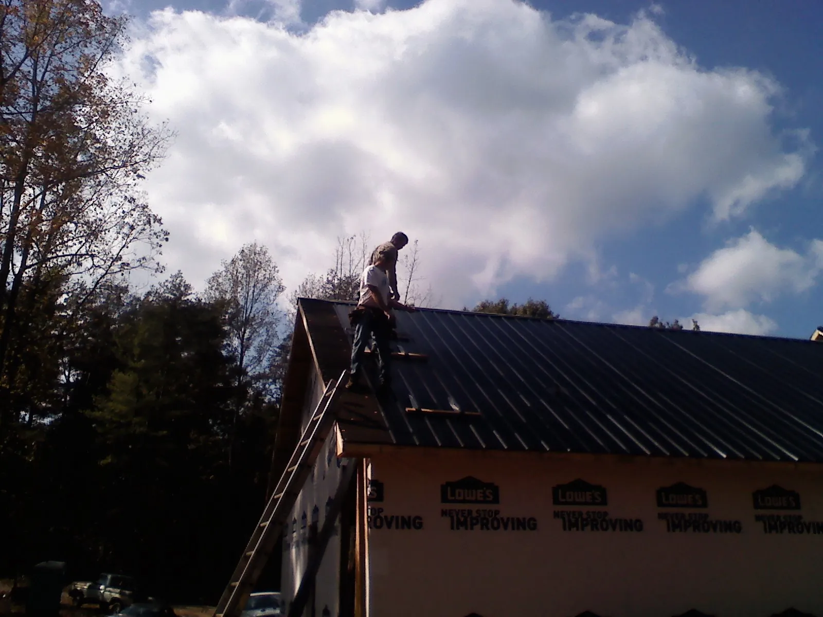 Roofer fastening dark metal panels high against a cloudy sky, from a Roof Inspection job in Unicoi