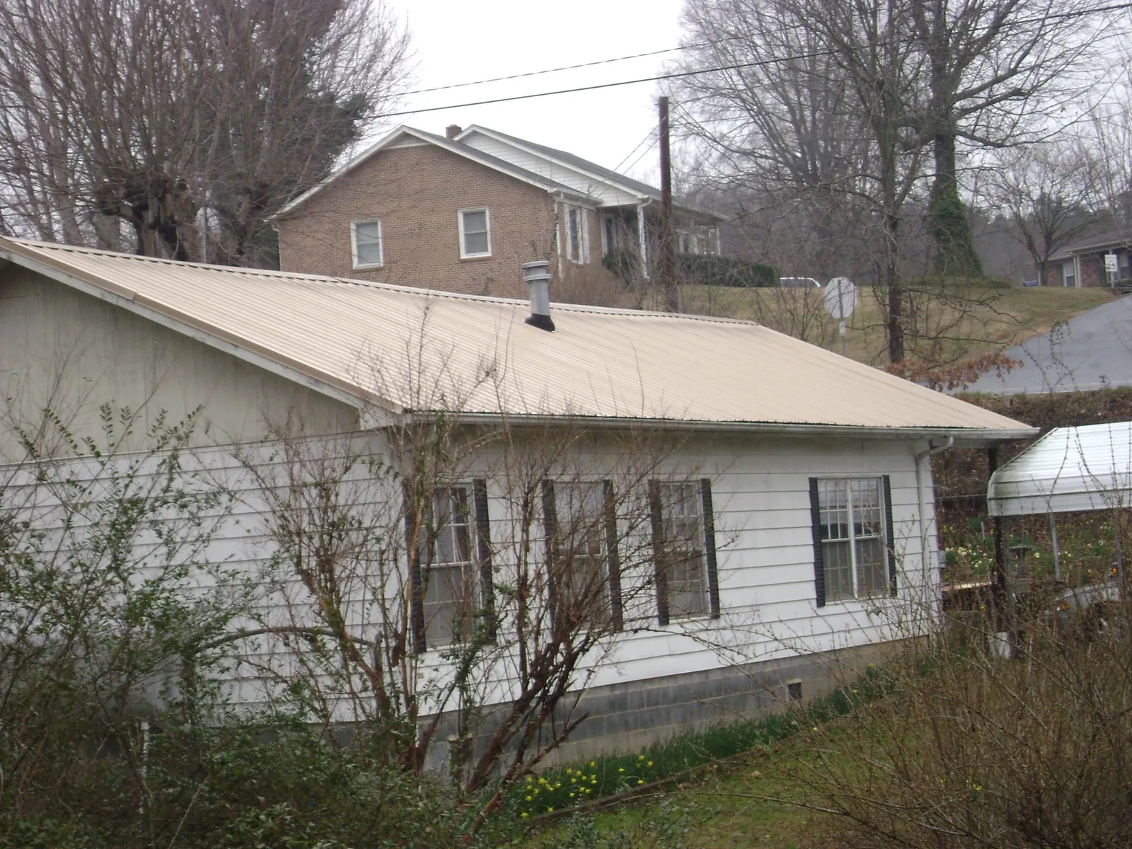 Tan metal roof on a white sided house set into a hillside — Commercial Roofing by Roofing Brothers in Unicoi