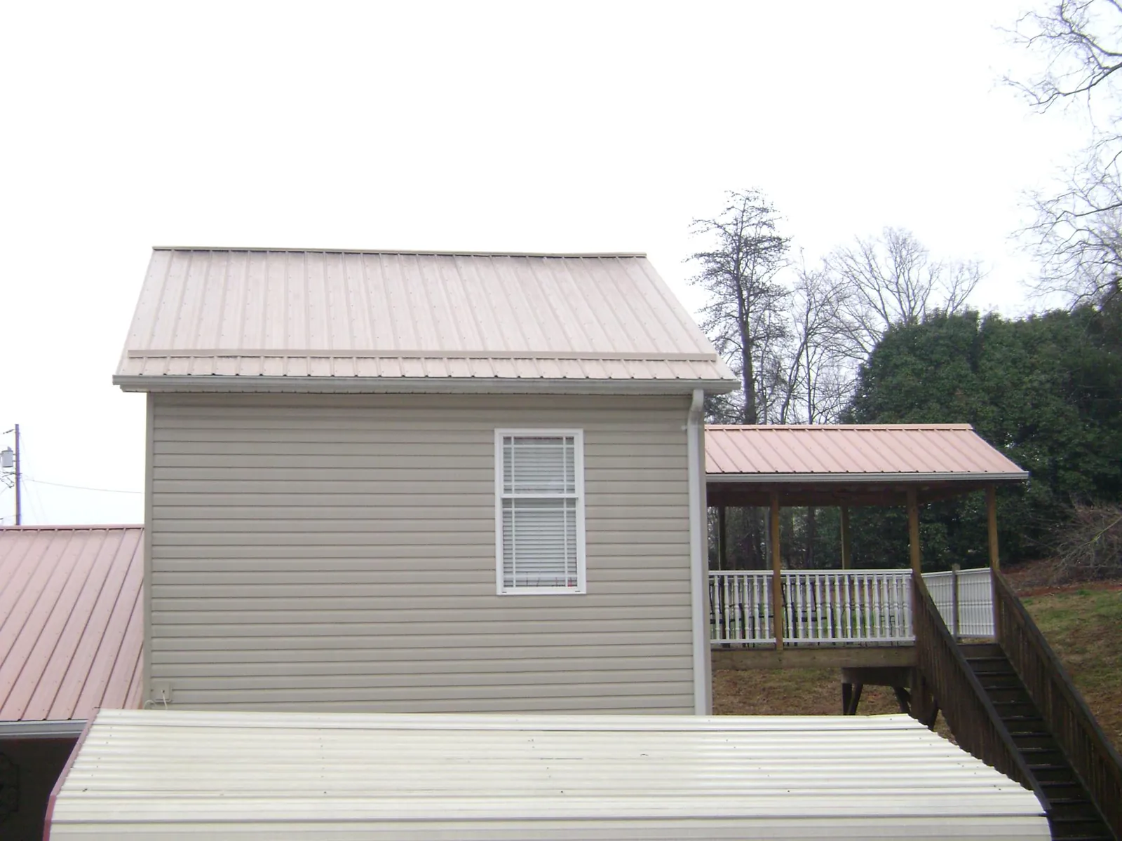 Tan metal roofs on a two story addition and attached porch, from a Roof Replacement job in Unicoi